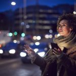 Woman On City Street At Night Ordering Taxi Using Mobile Phone App- taxisäkerhet och hög kvalitet blogg post